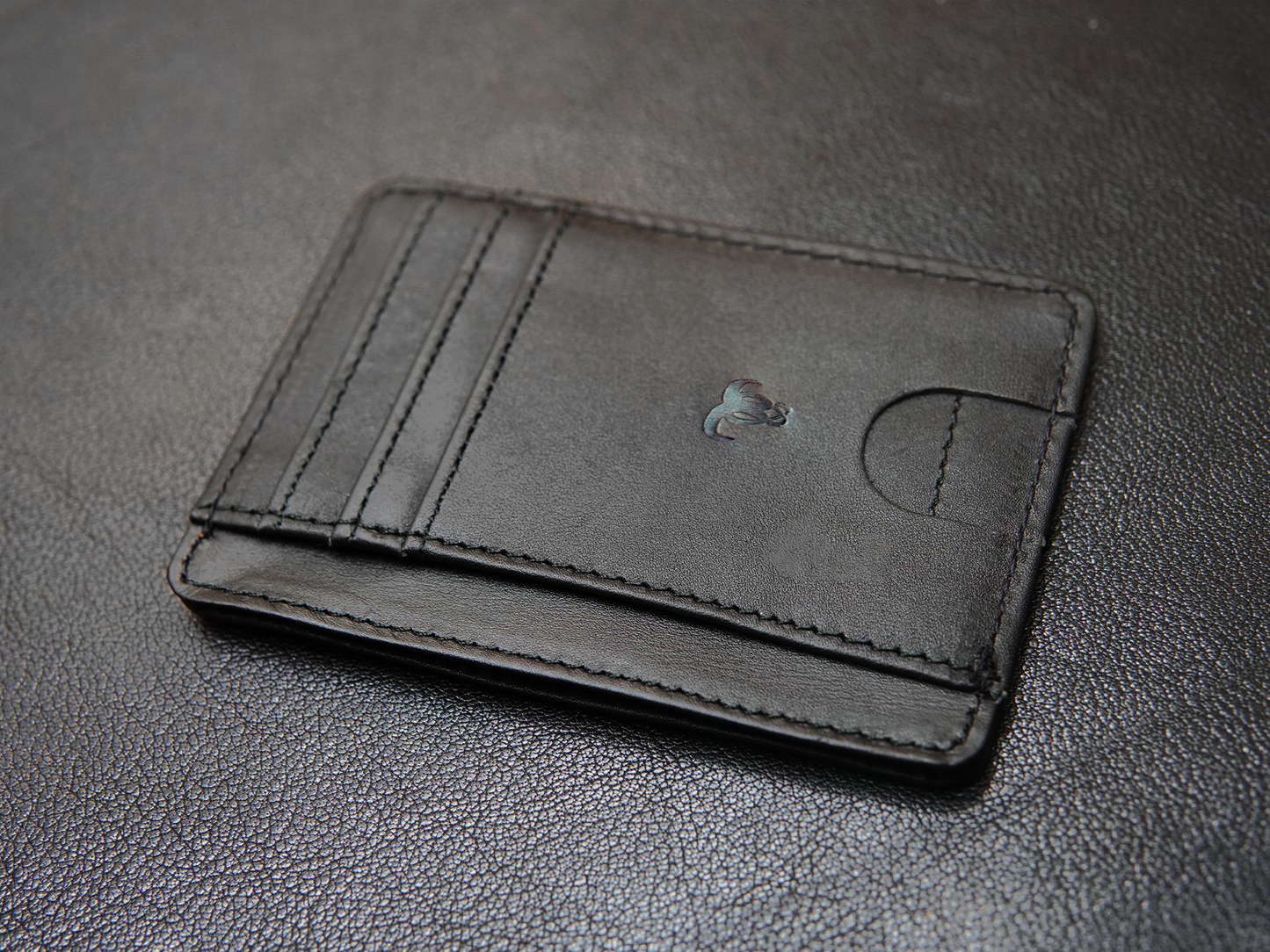 Flat layout of slim black leather card holder with ID window and cash pocket