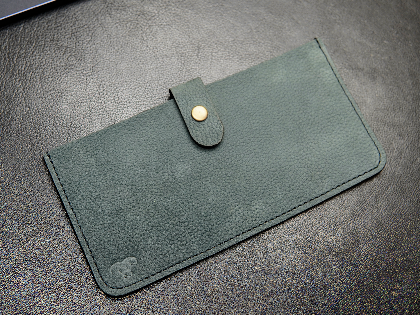 Close-up of button closure on green leather phone pouch