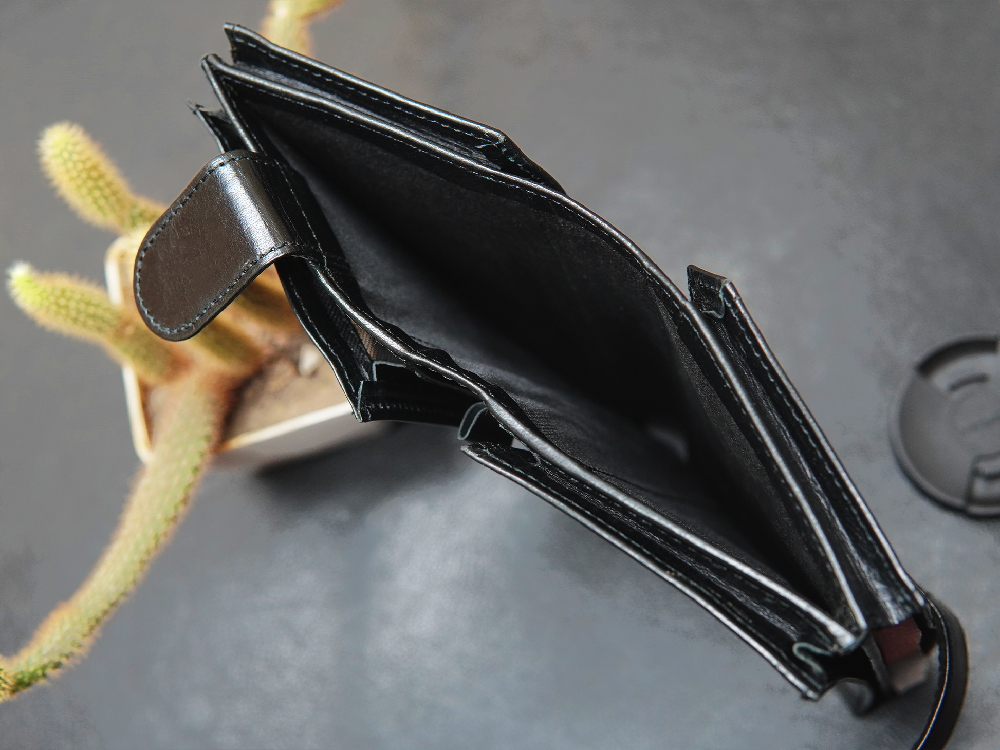 Black leather wallet on a gray surface with a blurred plant in the background