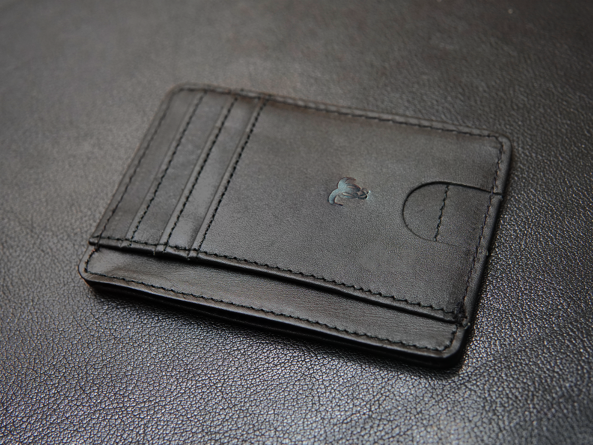 Flat layout of slim black leather card holder with ID window and cash pocket